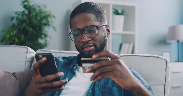 Man sitting on sofa using card to make online purchase on phone